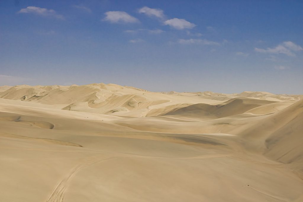 Serene aerial view of rolling sand dunes under a clear blue sky in the Namibian desert.
